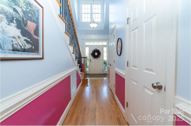 doorway to outside featuring a wealth of natural light, a towering ceiling, light wood-style flooring, and stairs