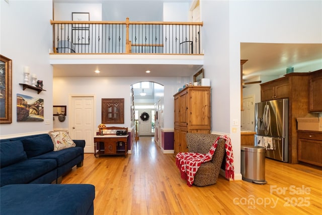 living area featuring light wood-style floors, arched walkways, and a high ceiling