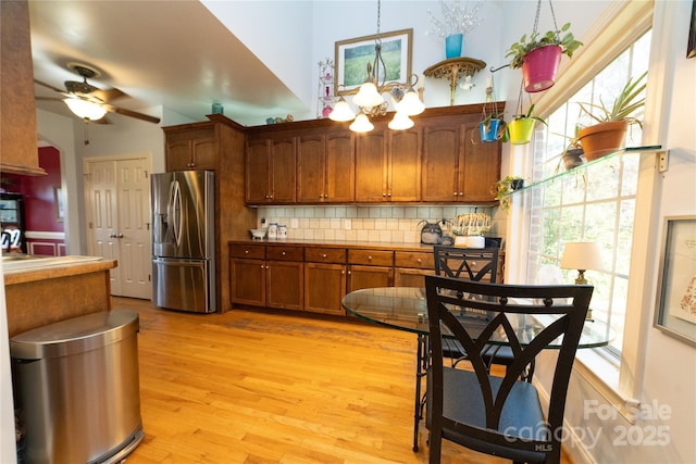 kitchen with brown cabinetry, light wood finished floors, stainless steel fridge with ice dispenser, arched walkways, and decorative backsplash