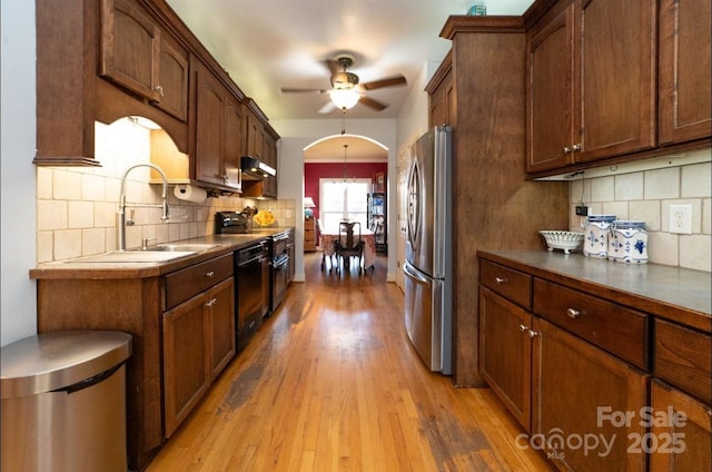 kitchen featuring light wood-style flooring, arched walkways, freestanding refrigerator, a sink, and dishwasher