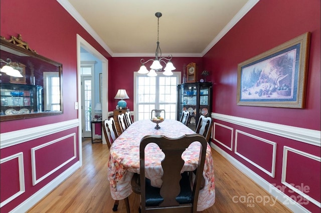 dining space featuring a chandelier, wood finished floors, ornamental molding, and wainscoting