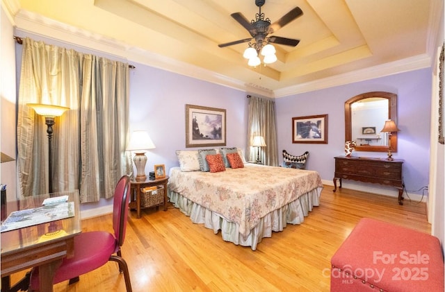 bedroom featuring crown molding, baseboards, light wood-type flooring, and a tray ceiling