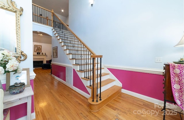 stairway featuring baseboards, a high ceiling, wood finished floors, and a fireplace