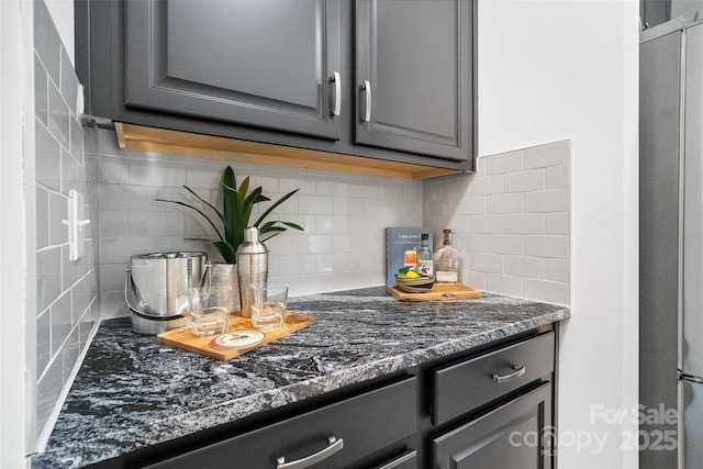 kitchen with tasteful backsplash, freestanding refrigerator, dark stone counters, and gray cabinetry