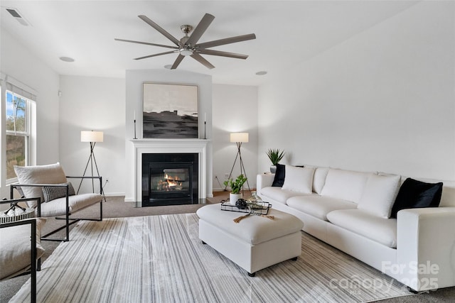 carpeted living room featuring a fireplace with flush hearth, visible vents, baseboards, and a ceiling fan