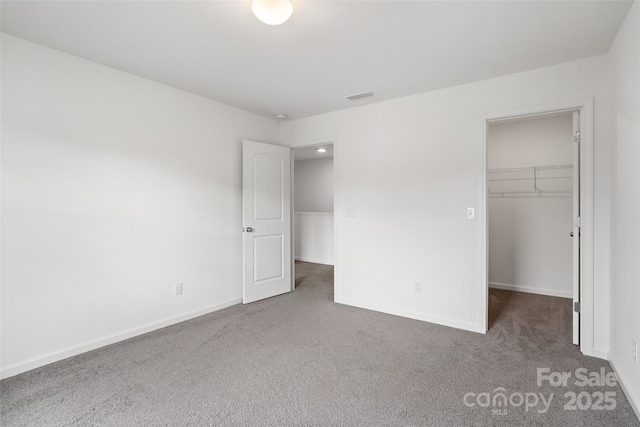 unfurnished bedroom featuring carpet, visible vents, a walk in closet, and baseboards