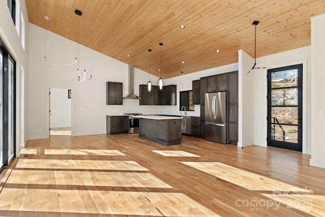 kitchen with wall chimney range hood, a high ceiling, appliances with stainless steel finishes, and a center island