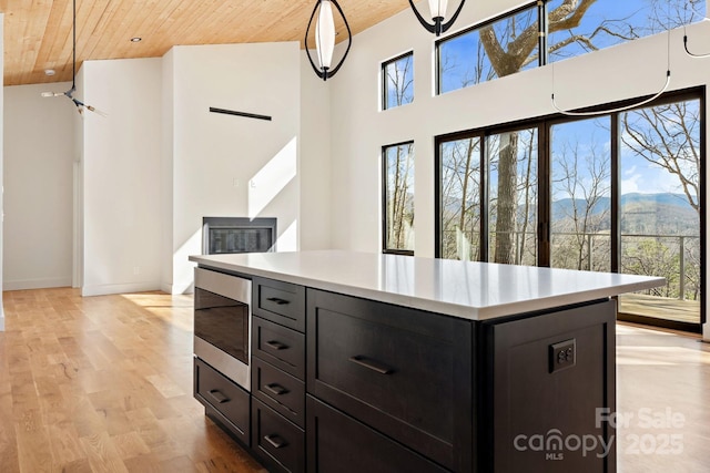 kitchen with a towering ceiling, wood ceiling, light wood-style flooring, stainless steel microwave, and light countertops