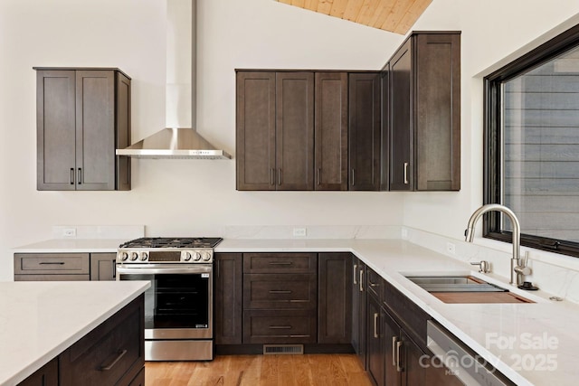 kitchen with visible vents, lofted ceiling, wall chimney exhaust hood, appliances with stainless steel finishes, and a sink