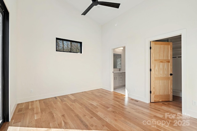 unfurnished bedroom featuring baseboards, connected bathroom, wood finished floors, a walk in closet, and a closet