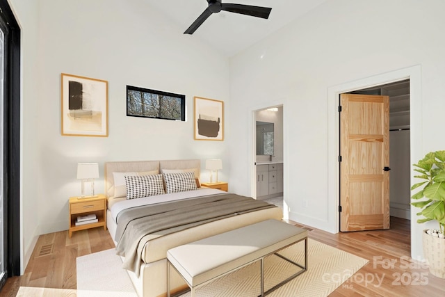 bedroom with ensuite bathroom, light wood finished floors, a walk in closet, and baseboards