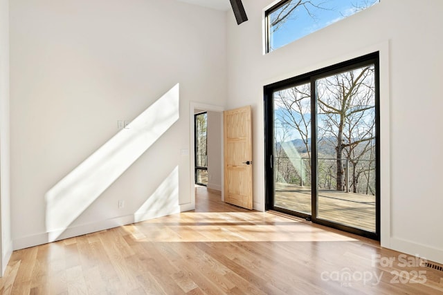 doorway to outside featuring visible vents, a high ceiling, light wood-style flooring, and baseboards