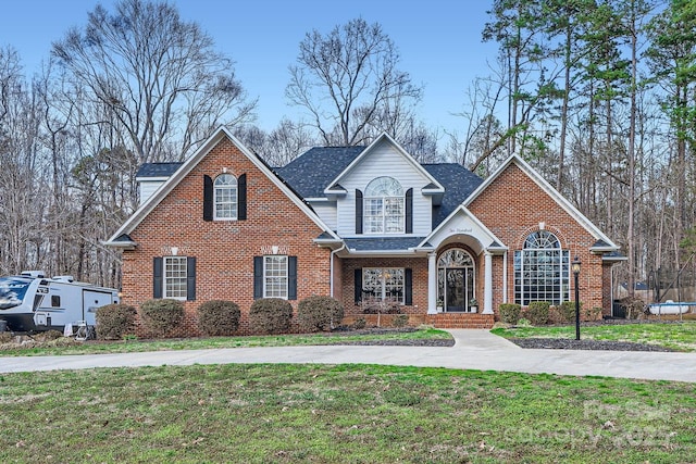 traditional-style home featuring concrete driveway, brick siding, roof with shingles, and a front yard