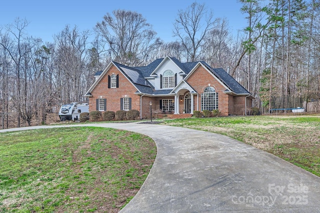 traditional-style house with a trampoline, a front yard, concrete driveway, and brick siding