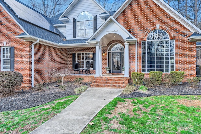 property entrance featuring roof with shingles and brick siding