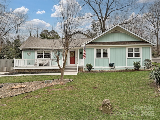 single story home with a porch, roof with shingles, a front yard, and fence