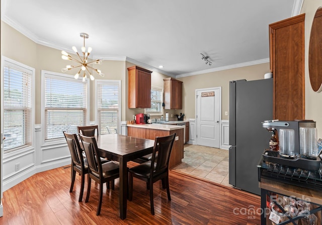 dining area with a wainscoted wall, ornamental molding, light wood-style floors, an inviting chandelier, and a decorative wall