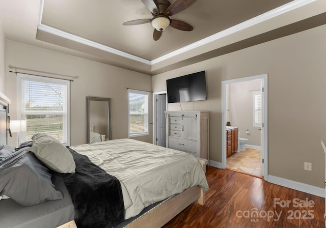 bedroom with multiple windows, a raised ceiling, baseboards, and wood finished floors