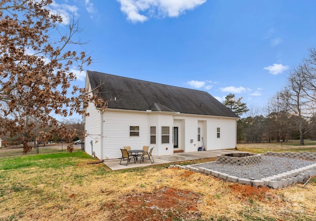 rear view of house featuring a patio, a lawn, roof with shingles, and an outdoor fire pit