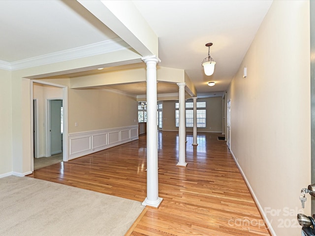 foyer entrance with crown molding, light wood-style flooring, a decorative wall, and ornate columns