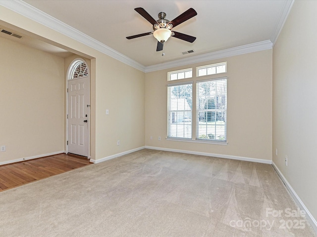 carpeted empty room with ceiling fan, visible vents, baseboards, and ornamental molding