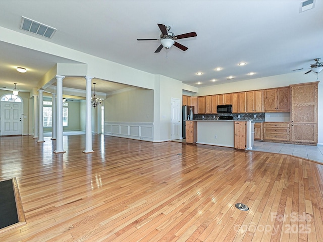 unfurnished living room with light wood-style flooring, decorative columns, ceiling fan with notable chandelier, and visible vents