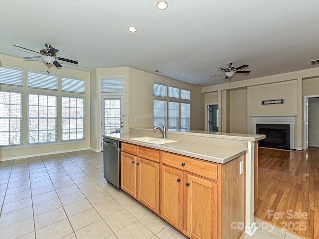 kitchen with a sink, ceiling fan, open floor plan, light countertops, and stainless steel dishwasher