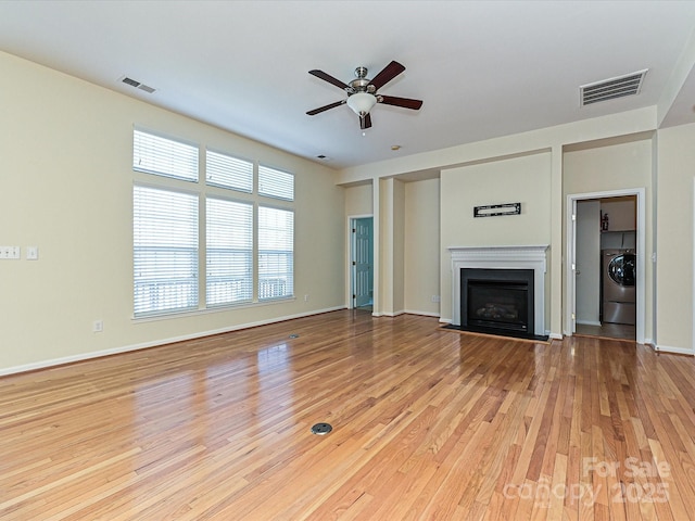 unfurnished living room with visible vents, a fireplace with flush hearth, washer / dryer, and wood finished floors