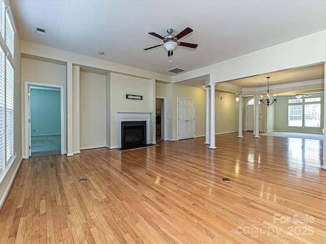 unfurnished living room featuring visible vents, ceiling fan with notable chandelier, light wood-style floors, a fireplace, and decorative columns