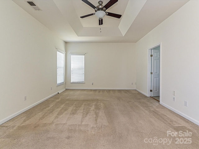 empty room with visible vents, light colored carpet, a raised ceiling, and baseboards