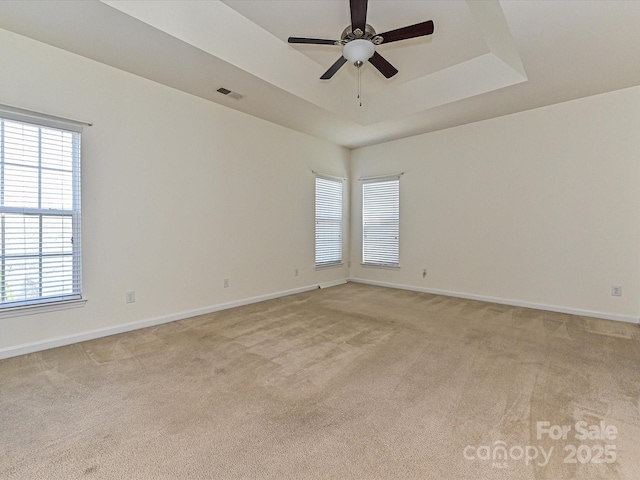 spare room featuring a ceiling fan, baseboards, visible vents, a tray ceiling, and light carpet