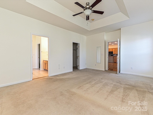 unfurnished bedroom featuring light colored carpet, baseboards, a raised ceiling, and a walk in closet