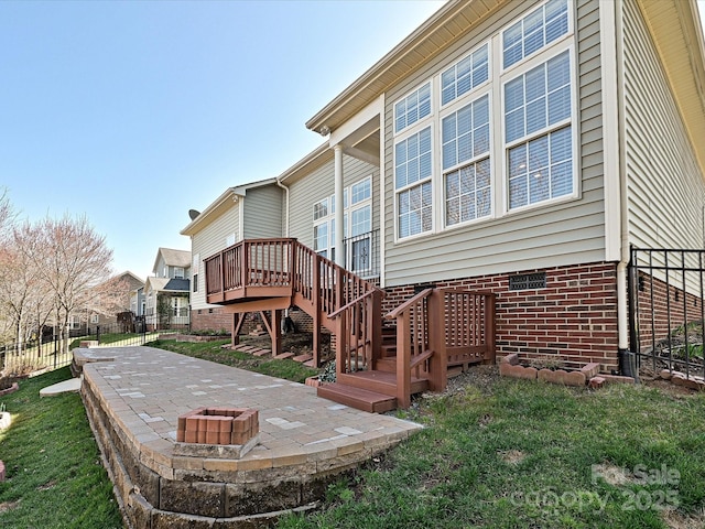 rear view of house featuring a patio, fence, a fire pit, a wooden deck, and brick siding