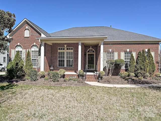 view of front of home featuring brick siding, covered porch, a front yard, and roof with shingles