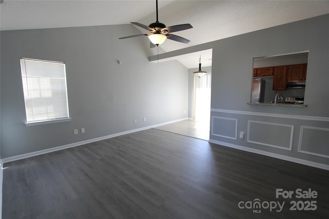 unfurnished living room with vaulted ceiling, ceiling fan, dark wood finished floors, and baseboards