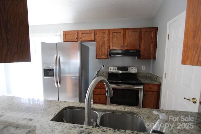 kitchen with brown cabinetry, light stone counters, stainless steel appliances, under cabinet range hood, and a sink