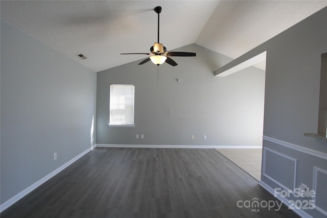 spare room with baseboards, visible vents, ceiling fan, dark wood-type flooring, and vaulted ceiling