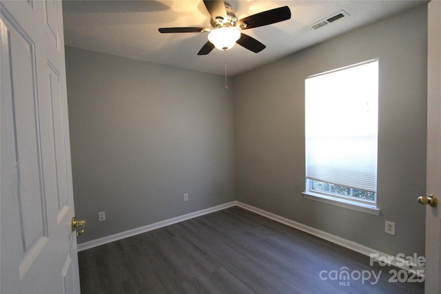 empty room with dark wood-style floors, visible vents, a textured ceiling, and baseboards