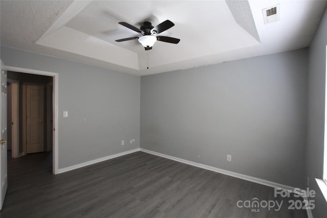 empty room featuring a tray ceiling, visible vents, dark wood-type flooring, ceiling fan, and baseboards