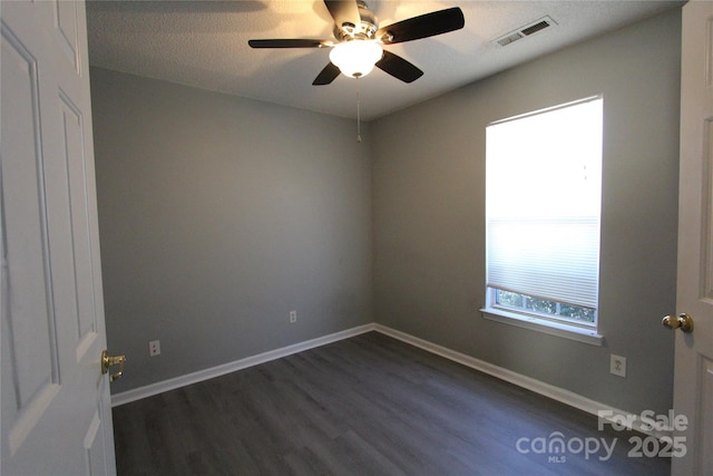 spare room featuring dark wood-style flooring, visible vents, and baseboards