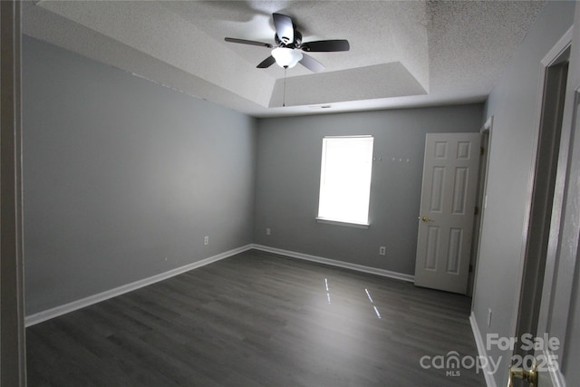 empty room featuring a raised ceiling, dark wood-type flooring, ceiling fan, a textured ceiling, and baseboards