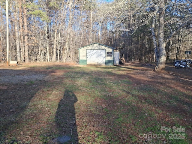 view of yard with a forest view, a detached garage, a storage unit, and an outdoor structure