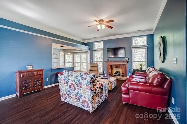 living area featuring wood finished floors, baseboards, a ceiling fan, a fireplace, and crown molding