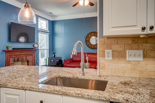 kitchen with crown molding, light stone countertops, decorative backsplash, white cabinetry, and a sink