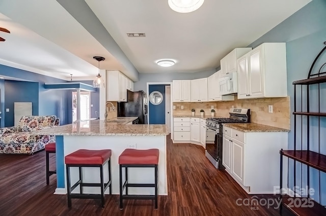 kitchen featuring stainless steel gas range oven, a sink, freestanding refrigerator, a peninsula, and white microwave