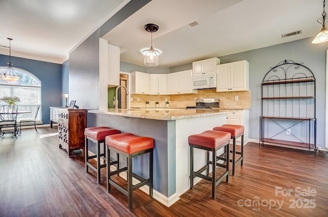 kitchen featuring white microwave, visible vents, stainless steel electric stove, a breakfast bar area, and light stone counters