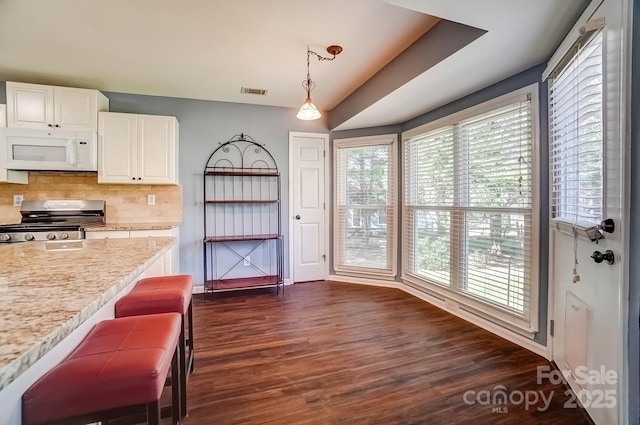 kitchen with dark wood-style floors, white microwave, stainless steel range oven, white cabinetry, and backsplash