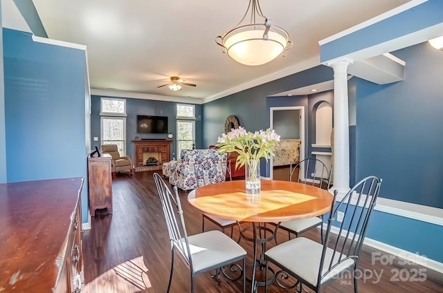 dining space with dark wood finished floors, a fireplace, decorative columns, baseboards, and ceiling fan