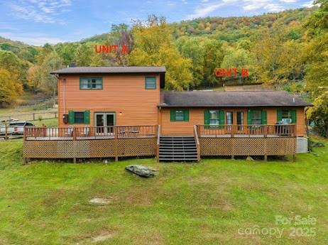 back of property with a wooden deck, a view of trees, and a lawn