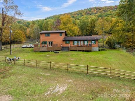 exterior space with a rural view, a forest view, fence, a wooden deck, and a lawn